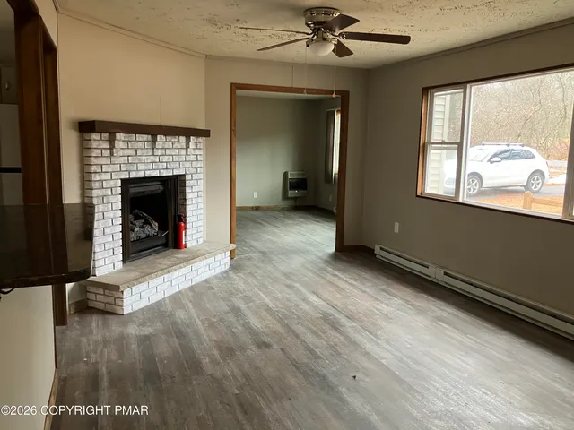 a view of an empty room with wooden floor fireplace and a window