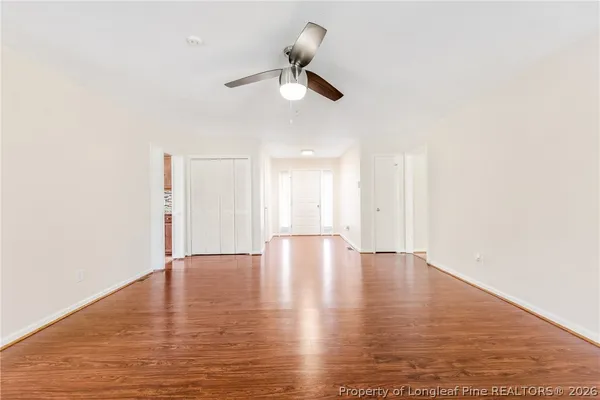 a view of an empty room with wooden floor and a ceiling fan