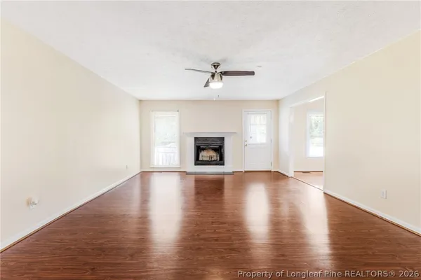 an empty room with wooden floor ceiling fan and windows