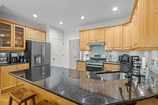 a kitchen with stainless steel appliances granite countertop a refrigerator a stove and a sink with wooden cabinets