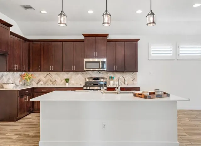 a kitchen with stainless steel appliances granite countertop wooden cabinets a sink a stove a refrigerator and island with wooden floor