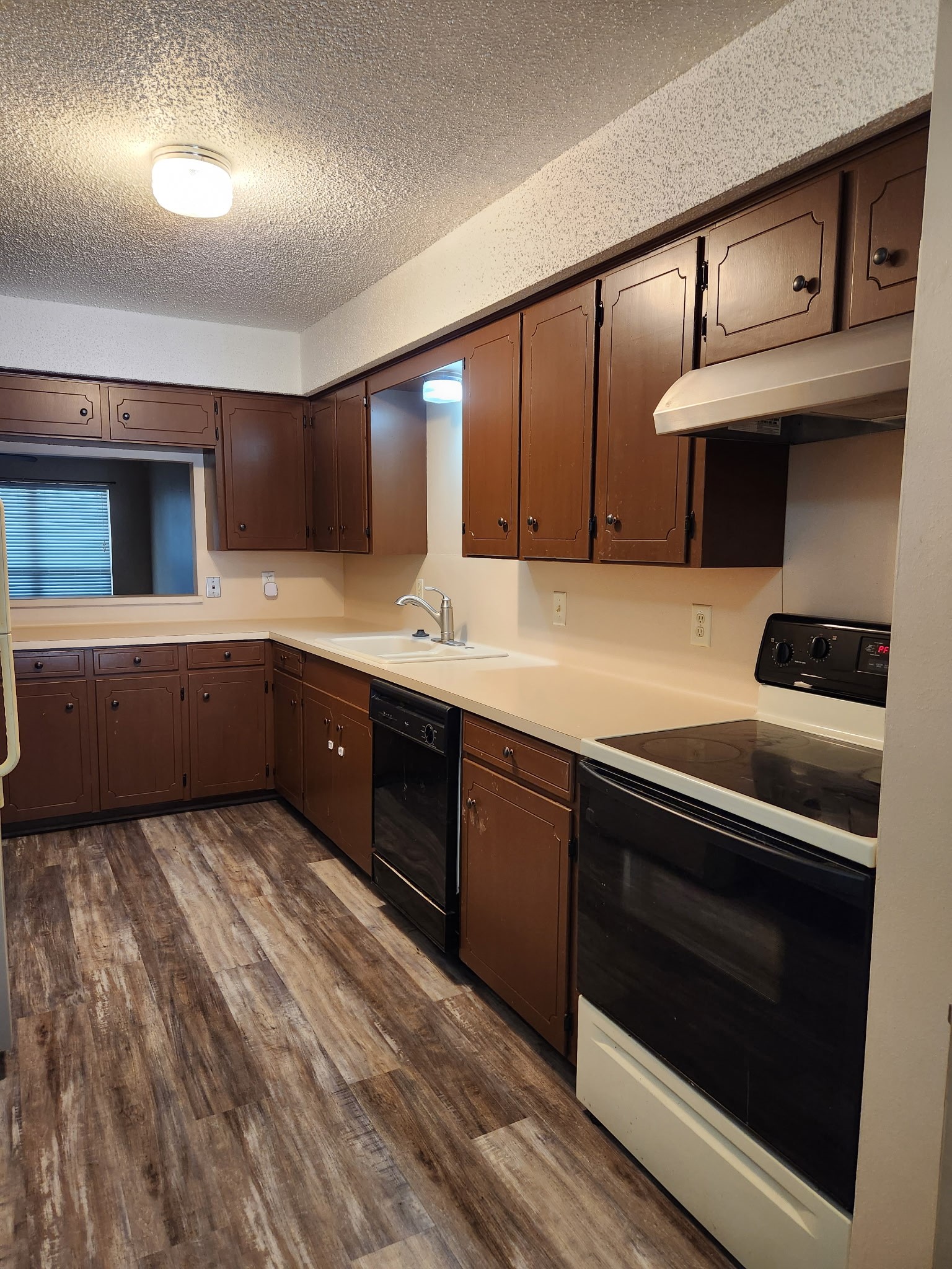 1252 Eagle Lake Road, Unit 8 Sealy, TX 77474 - Photo 7 of 18 This kitchen features dark wood cabinets, light countertops, and a mix of appliances. The space has a cozy feel with wood-style flooring and ample storage.