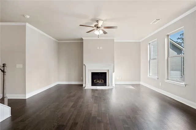 an empty room with wooden floor a ceiling fan a fireplace and windows