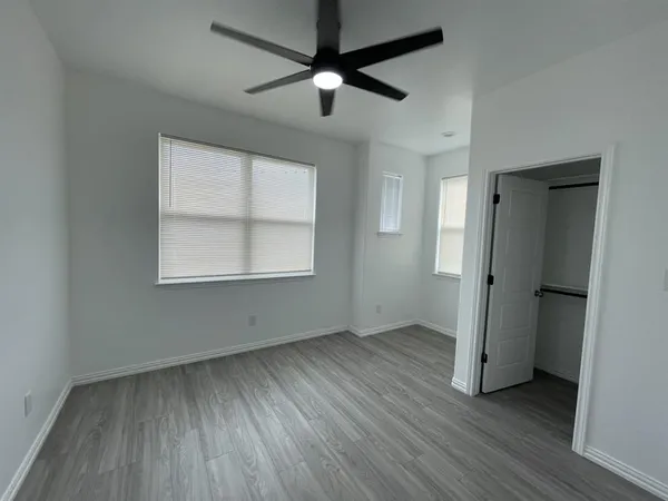 an empty room with wooden floor a ceiling fan and windows