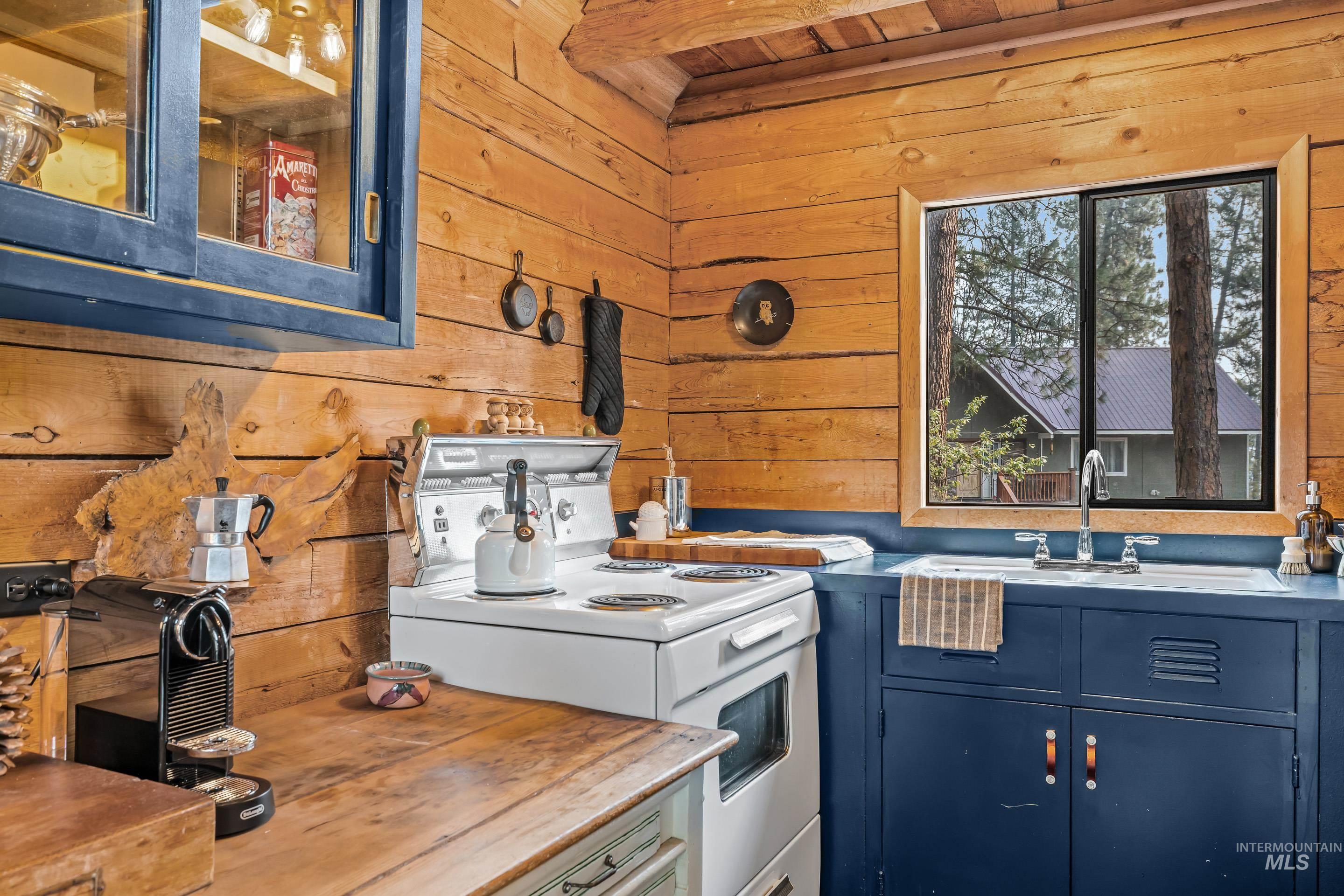 73 Rainbow Ridge Road Garden Valley, ID 83622 - Photo 11 of 49 Wood-paneled walls and ceiling, wood-finish countertops, built-in blue cabinetry, white enamel sink, and a white range