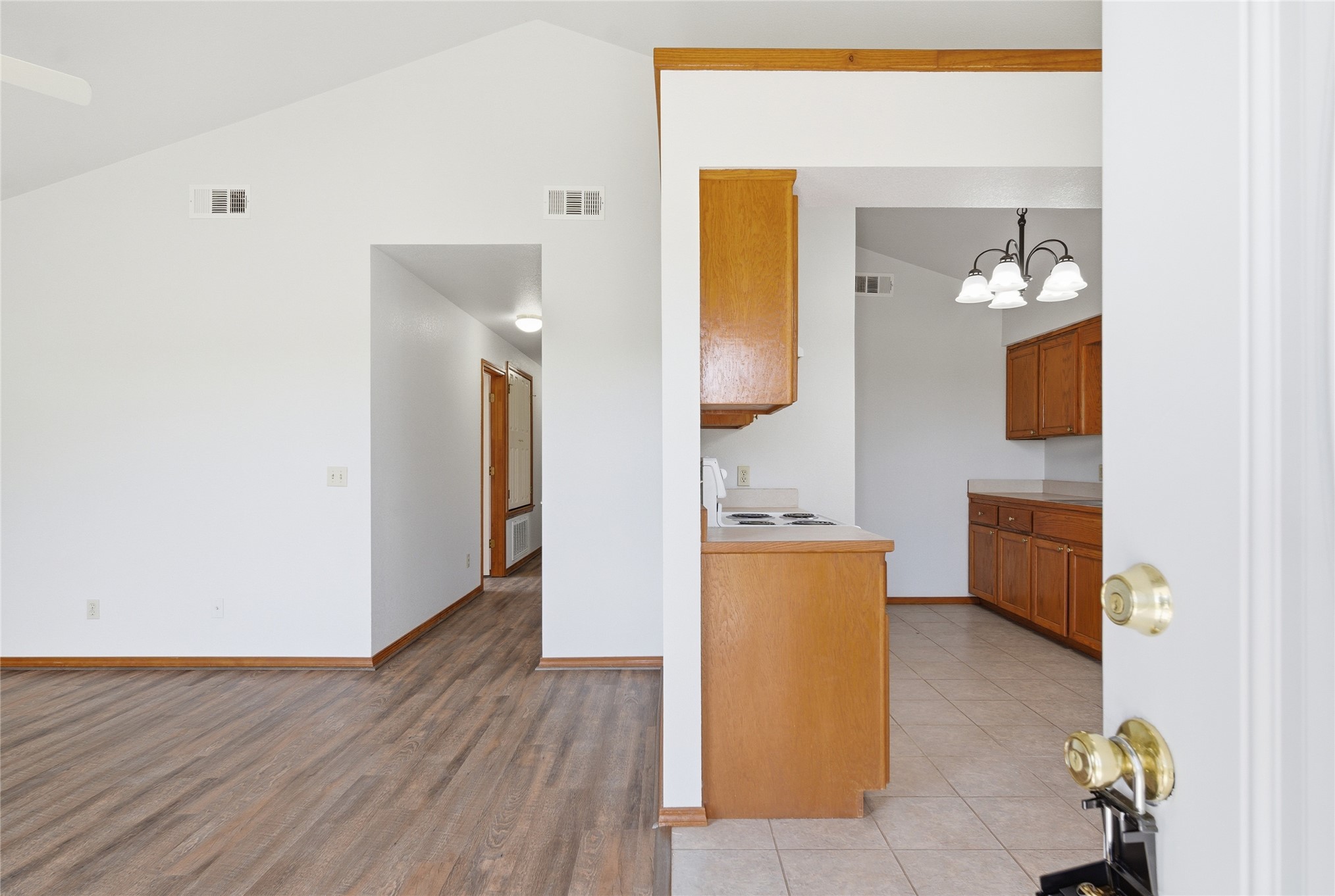 Vaulted ceiling, wood-finish flooring, light wood cabinetry, tile flooring, and a ceiling fan