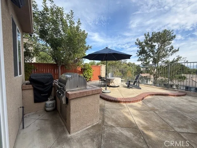 a view of a patio with table and chairs under an umbrella with large trees