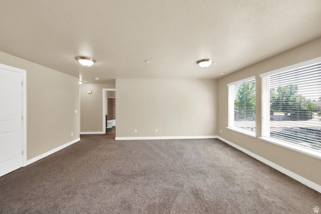 909 South Main Street, Unit G Layton, UT 84041 - Photo 6 of 25 Spacious room featuring neutral paint, brown carpet, two windows with blinds, a white paneled door, and two flush-mount ceiling lights
