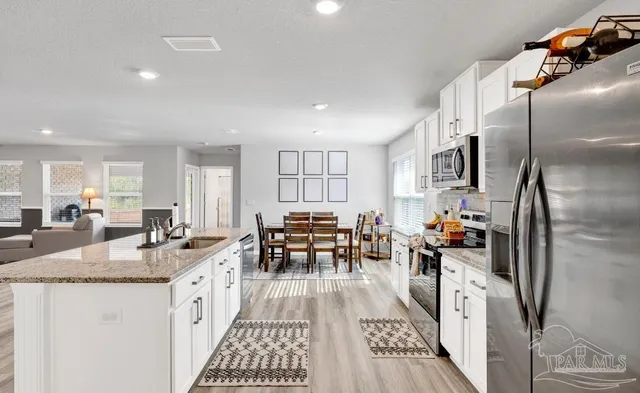 a kitchen with stainless steel appliances granite countertop a refrigerator a sink dishwasher a dining table and chairs with wooden floor