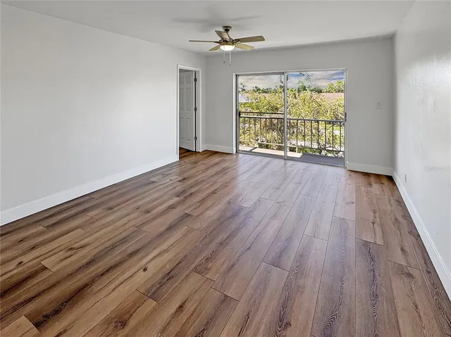 an empty room with wooden floor chandelier fan and windows