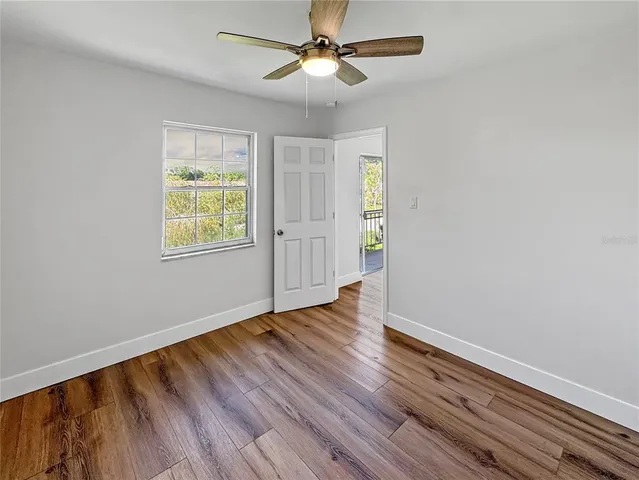 an empty room with wooden floor ceiling fan and windows