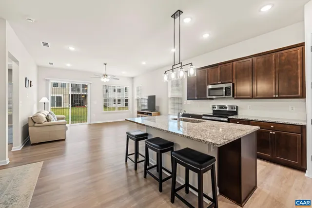 a kitchen with stainless steel appliances granite countertop a stove top oven a sink dishwasher a dining table and chairs with wooden floor