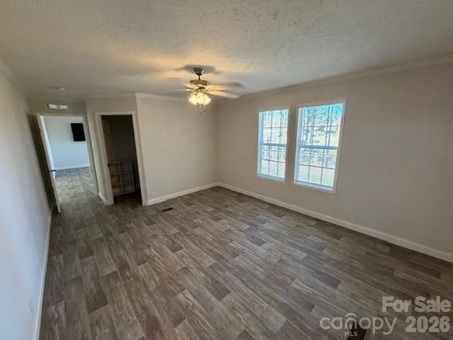 an empty room with wooden floor chandelier fan and windows
