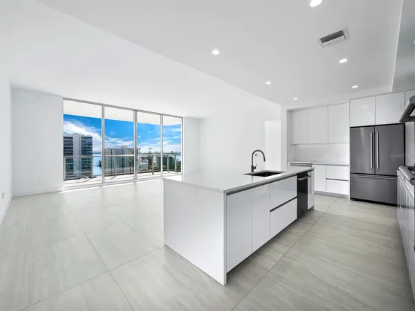 a large white kitchen with kitchen island a large counter top and stainless steel appliances