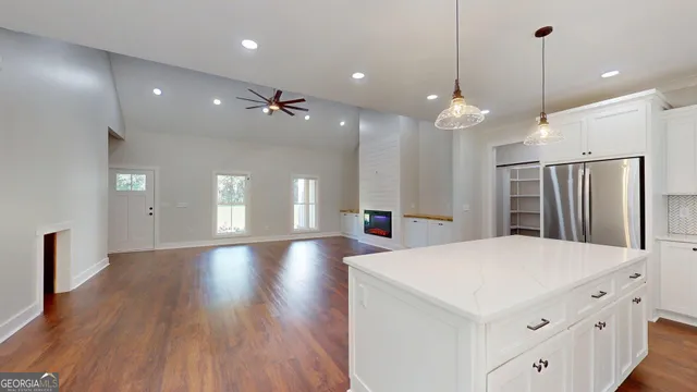 a large white kitchen with a large island oven a stove white cabinetry and couches with wooden floor