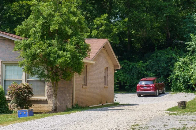 a car parked in front of a white house with large trees