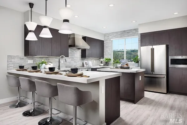 a kitchen with stainless steel appliances a sink a stove a refrigerator cabinets and chairs