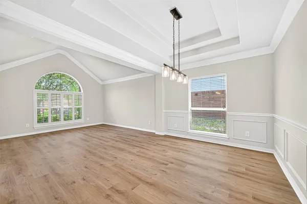 a view of an empty room with wooden floor kitchen view and a window