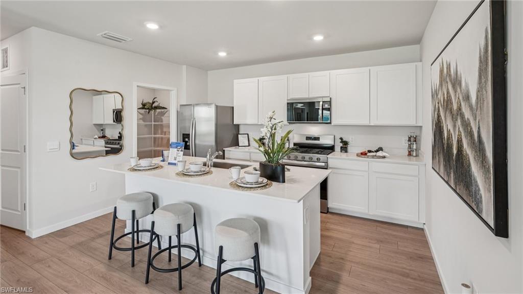 17625 Shade Tree Loop Babcock Ranch, FL 33982 - Photo 8 of 34 a kitchen with stainless steel appliances a sink a stove a refrigerator cabinets and a dining table with wooden floor