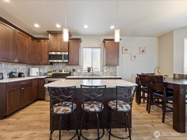 a kitchen with stainless steel appliances granite countertop a table chairs sink and cabinets