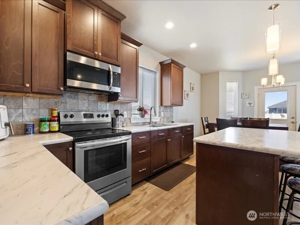 a kitchen with stainless steel appliances granite countertop a stove top oven a sink dishwasher and white cabinets with wooden floor