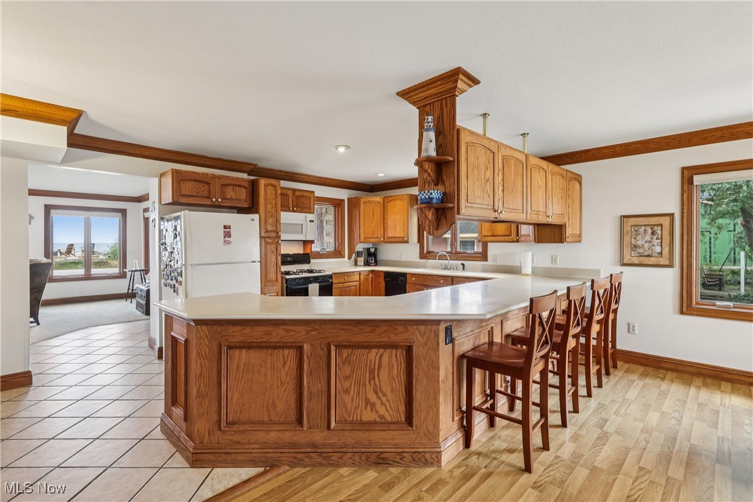 337 Cedar Point Road Sandusky, OH 44870 - Photo 12 of 50 Kitchen featuring light countertops, a peninsula, brown cabinets, white appliances, and a kitchen bar