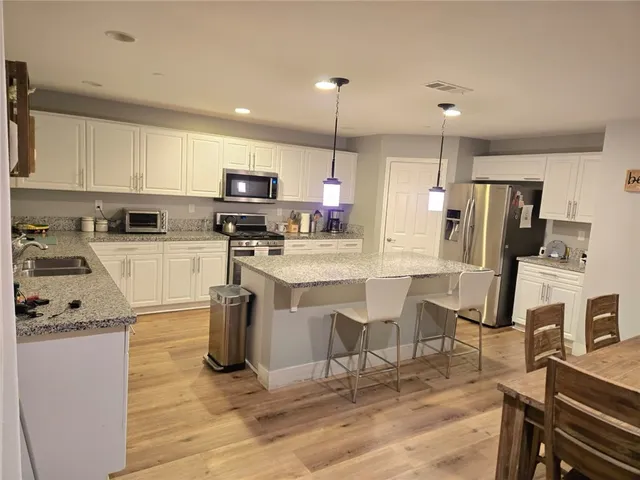 a kitchen with stainless steel appliances granite countertop a refrigerator a stove top oven a sink dishwasher a dining table and chairs with wooden floor