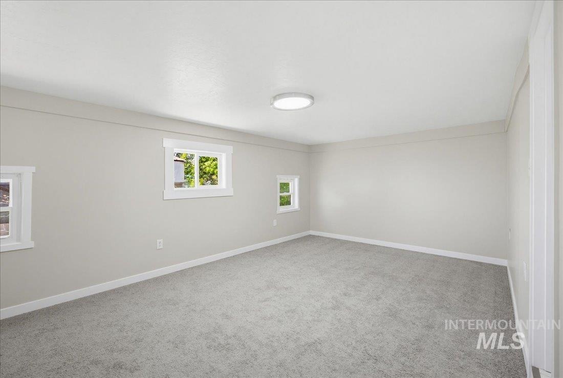 30013 Apple Valley Road Parma, ID 83660 - Photo 13 of 25 Spacious room featuring light gray carpeting, multiple windows with white trim, and a contemporary flush-mount ceiling light