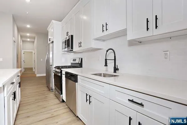 a kitchen with stainless steel appliances a sink dishwasher a stove and a refrigerator with wooden floor