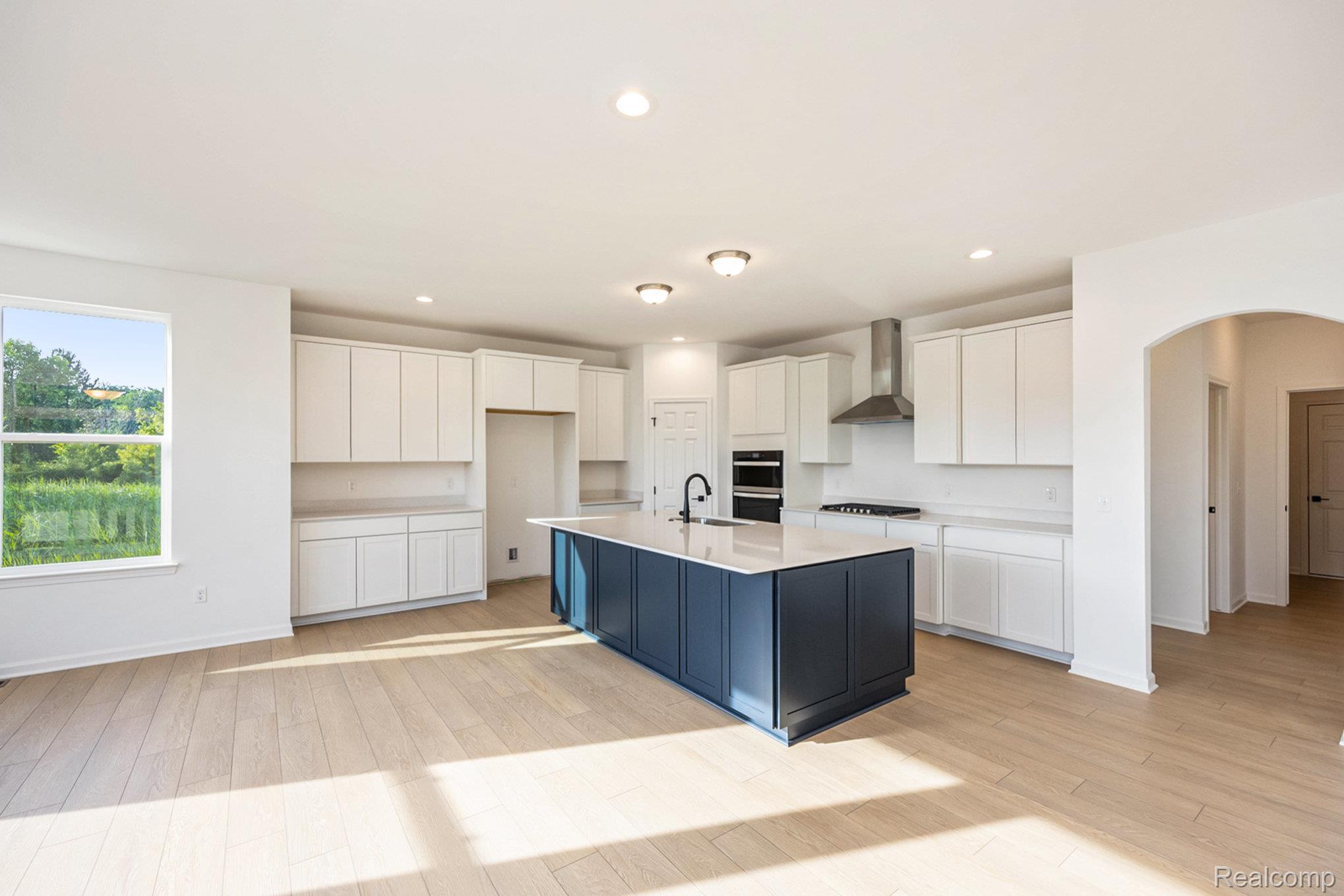 68788 Place Road New Haven, MI 48050 - Photo 6 of 29 Kitchen featuring white cabinetry, arched walkways, wall chimney exhaust hood, recessed lighting, and a kitchen island with sink