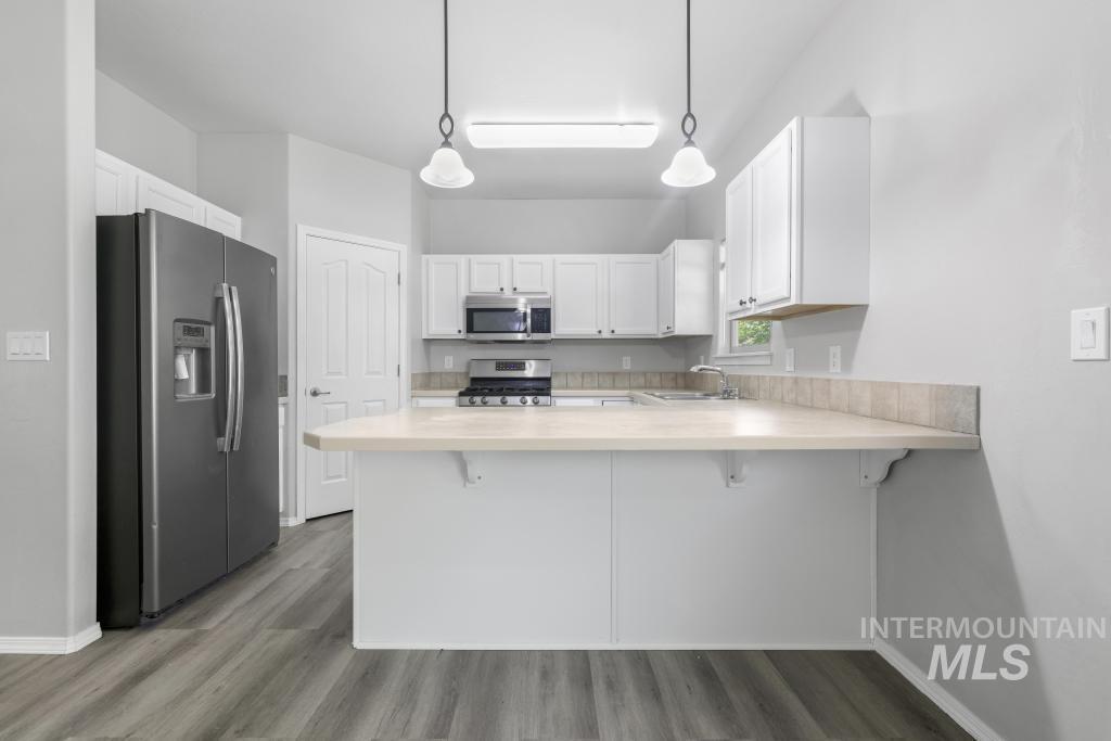 1183 Cortes Loop Twin Falls, ID 83301 - Photo 6 of 30 Kitchen featuring white cabinetry, stainless steel appliances, a breakfast bar, light-toned countertops, and wood-finish flooring