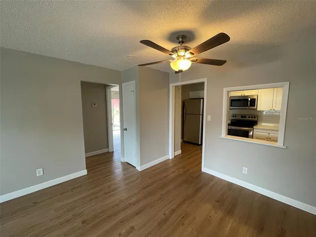 a view of an empty room with wooden floor and a ceiling fan