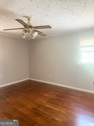 an empty room with wooden floor fan and windows