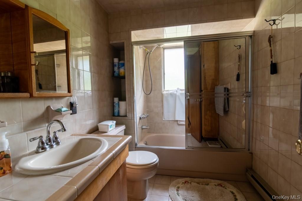 139 Haddock Road Monticello, NY 12701 - Photo 26 of 40 Bathroom with tile walls, a baseboard radiator, vanity, combined bath / shower with glass door, and tile patterned flooring
