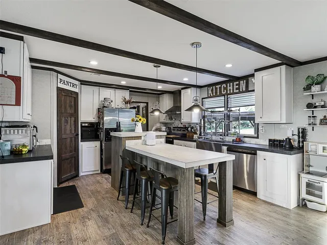 a kitchen with stainless steel appliances kitchen island granite countertop a refrigerator a stove a sink a dining table and chairs with wooden floor