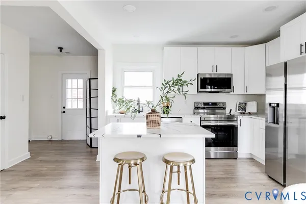 a kitchen with stainless steel appliances a stove a sink a refrigerator white cabinets and wooden floor