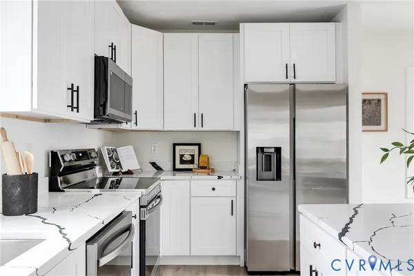 a kitchen with stainless steel appliances a refrigerator a sink a stove and white cabinets