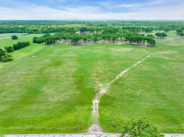 a view of a green field with lawn chairs and large trees