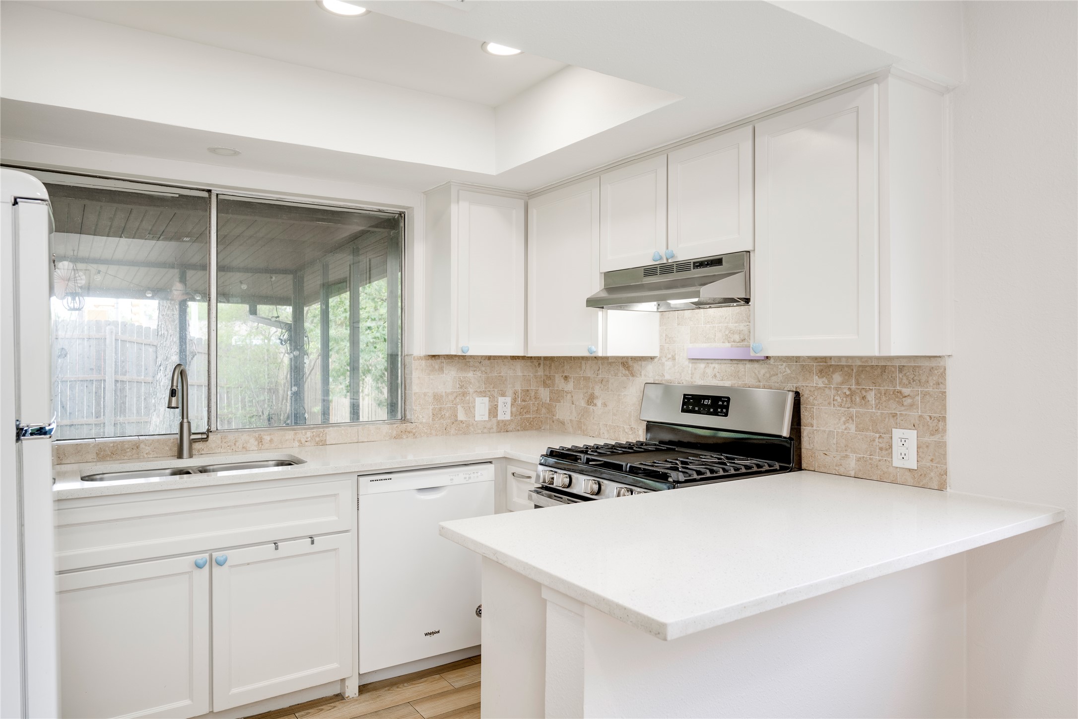 4811 Brushy Ridge Drive Austin, TX 78744 - Photo 23 of 39 Kitchen with white appliances, a peninsula, white cabinetry, light wood-style floors, and tasteful backsplash