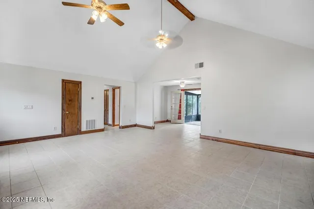 an empty room with chandelier fan and windows