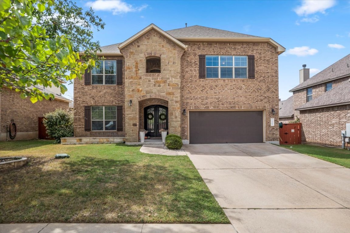 View of front of home featuring a front yard, concrete driveway, brick stone, and an attached garage