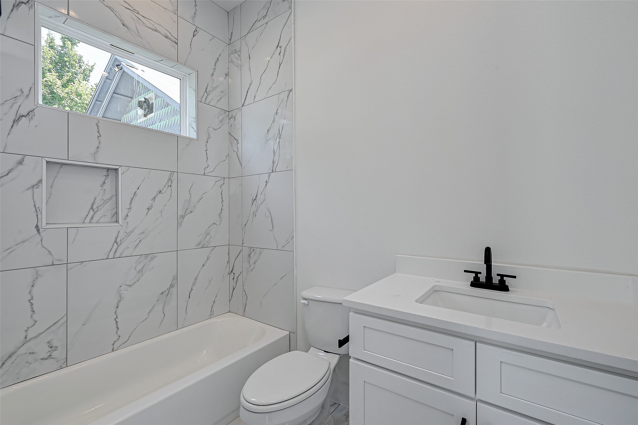 6032 Beall Street Houston, TX 77091 - Photo 11 of 26 The private bath features elegant marble-style tile, a soaking tub/shower combo, sleek matte black hardware, and a large niche for storage blending modern design with everyday comfort.