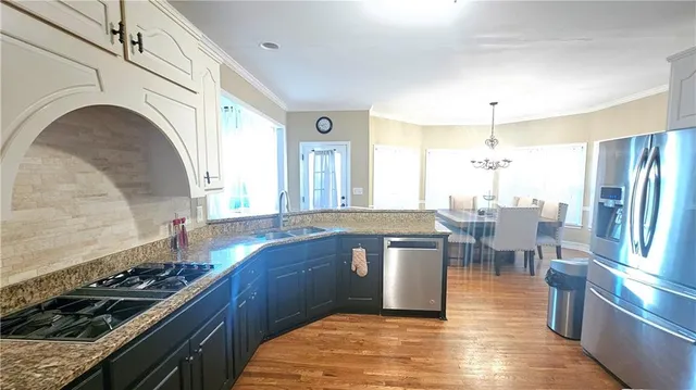 a kitchen with stainless steel appliances granite countertop a stove a sink dishwasher and a dining table with wooden floor
