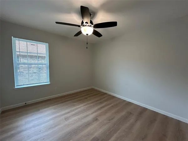 an empty room with wooden floor fan and windows
