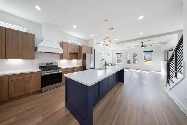 a large kitchen with stainless steel appliances a large counter top a sink a stove and a wooden floors