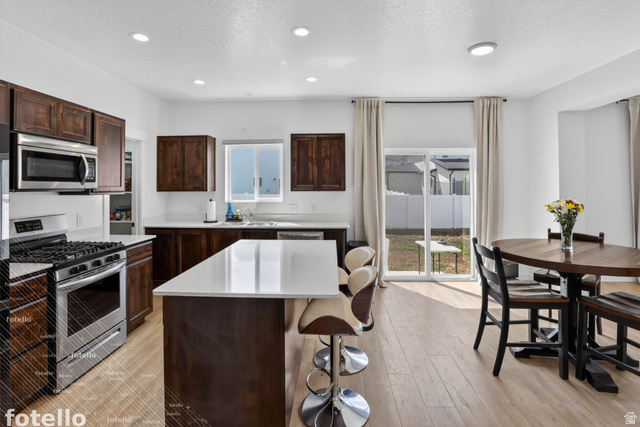 815 West Powderwood Lane Mapleton, UT 84664 - Photo 12 of 39 Kitchen featuring stainless steel appliances, dark wood finish cabinetry, a textured ceiling, a kitchen island, and light wood-type flooring