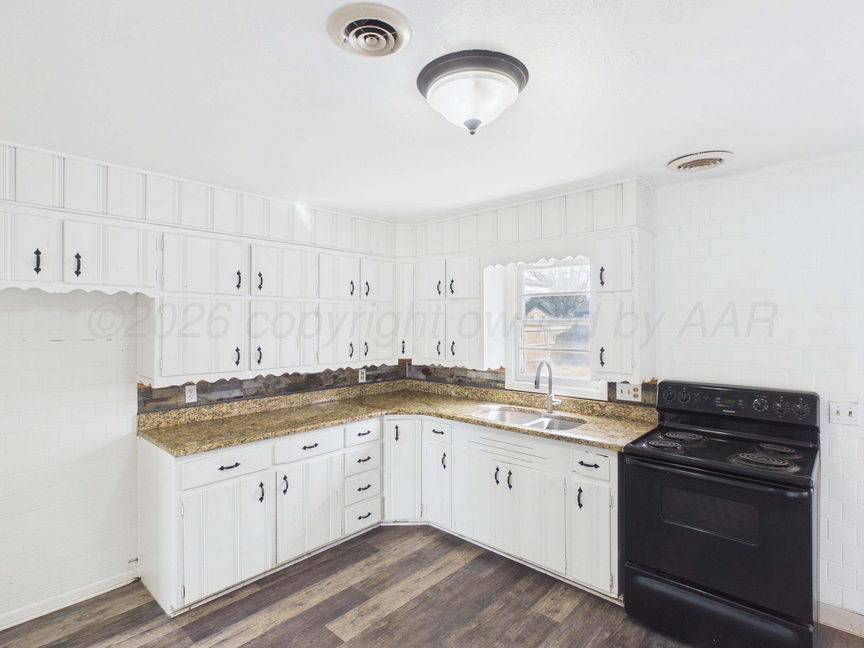 813 Northeast 3rd Street Dumas, TX 79029 - Photo 15 of 22 a white kitchen with a sink and dishwasher a stove with wooden floors