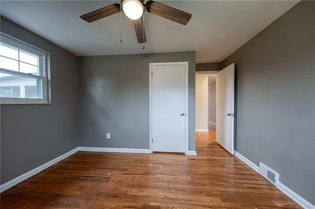 an empty room with wooden floor fan and windows
