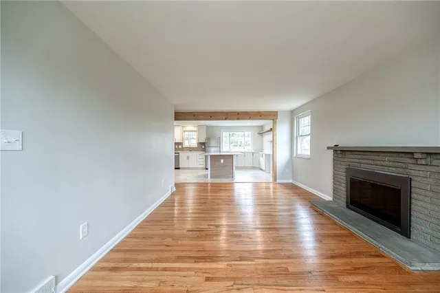 a view of an empty room with wooden floor fireplace and a window