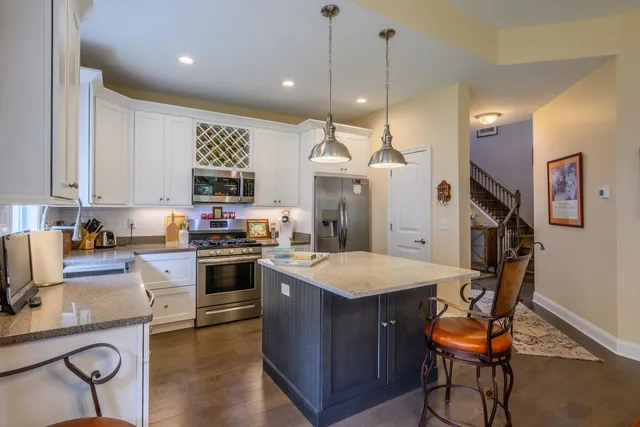 a kitchen with stainless steel appliances granite countertop a stove top oven a refrigerator a sink and chairs